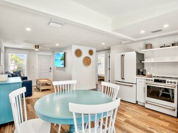 The image shows a modern kitchen and living space with wooden floors, white furniture, and decorative wall baskets, creating a cozy atmosphere.