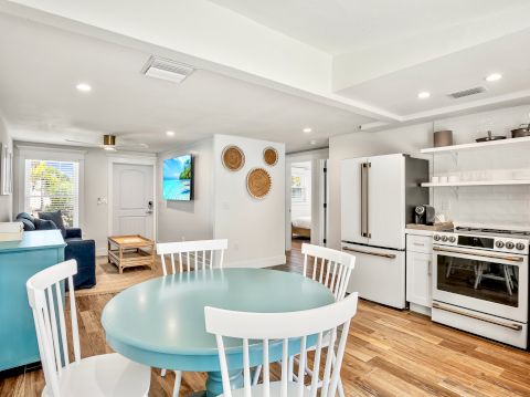 The image shows a modern kitchen and living space with wooden floors, white furniture, and decorative wall baskets, creating a cozy atmosphere.