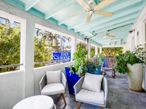 A cozy patio with seating, plants, ceiling fans, and a sign saying "Eden House." The space has a relaxed, welcoming atmosphere.