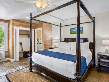 The image shows a bedroom with a canopy bed, nightstand, lamp, and open closet, featuring wooden accents and a ceiling fan.