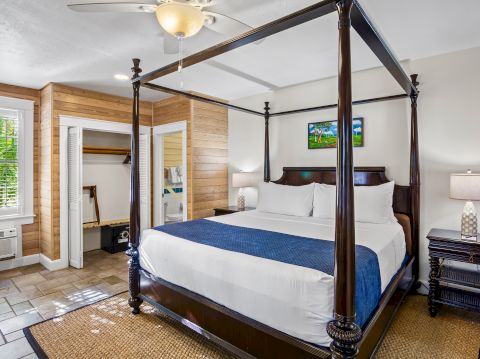 The image shows a bedroom with a canopy bed, nightstand, lamp, and open closet, featuring wooden accents and a ceiling fan.