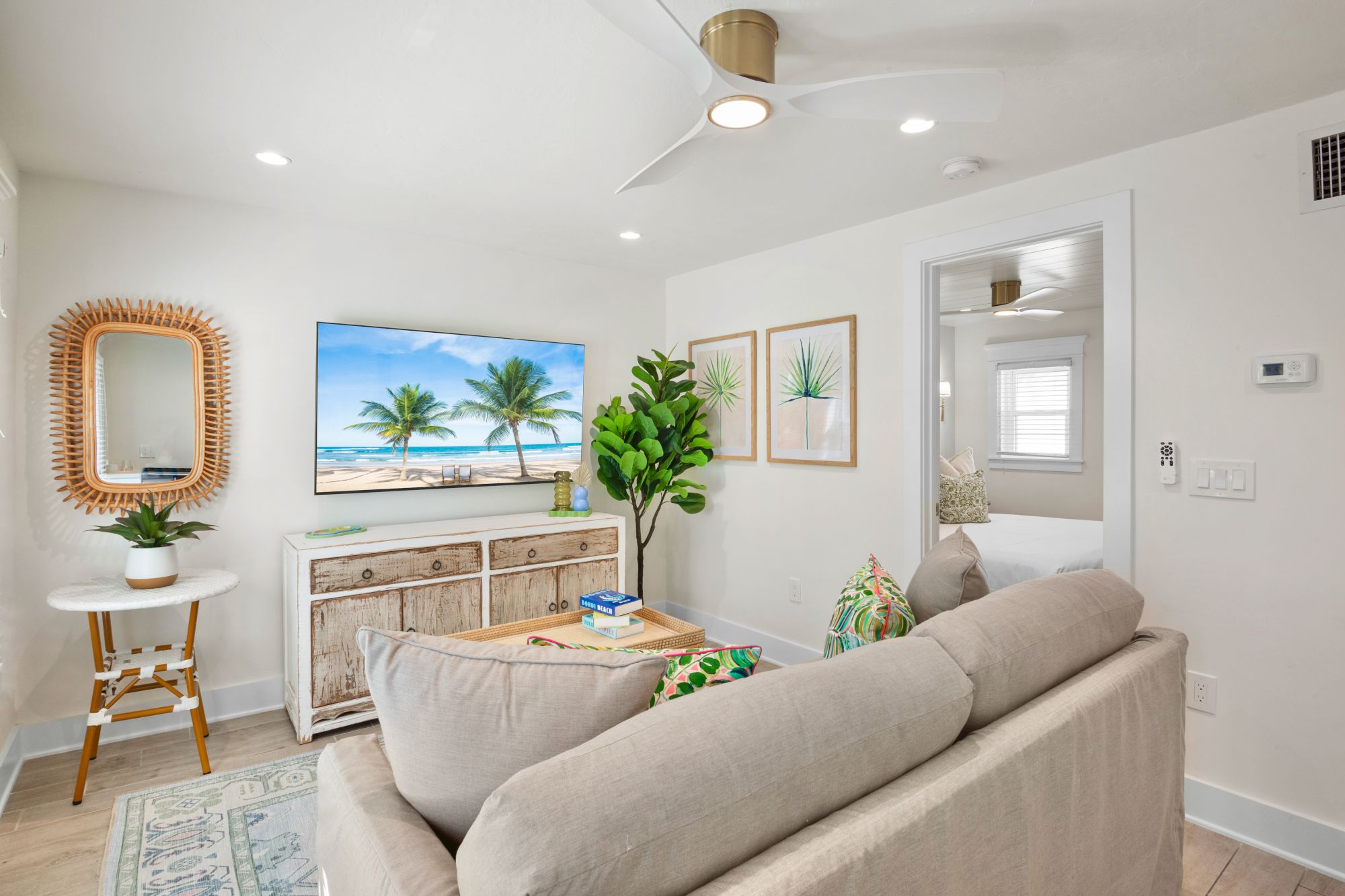 A cozy living room with a beige sofa, TV displaying a beach scene, wooden furniture, and green plants, creating a relaxed atmosphere.