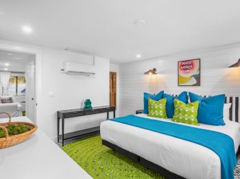 A modern bedroom features a neatly made bed with blue and green accents, wall art, and a basket with plants on a nearby surface.