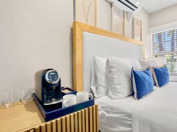 A cozy bedroom with a neatly made bed featuring blue pillows, a coffee machine, and cups on the bedside table, enhancing the comfort.