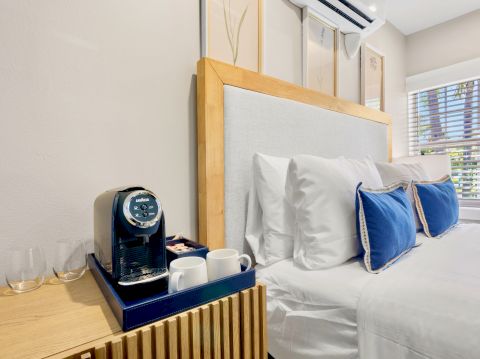 A cozy bedroom with a neatly made bed featuring blue pillows, a coffee machine, and cups on the bedside table, enhancing the comfort.