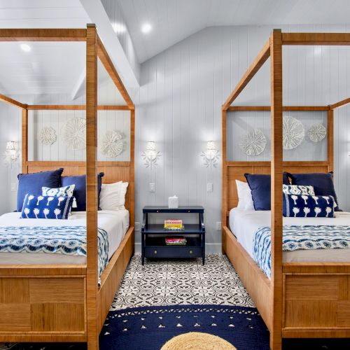 The image shows a bedroom with two wooden canopy beds, blue accents, patterned bedding, a central nightstand, and decorative wall hangings.