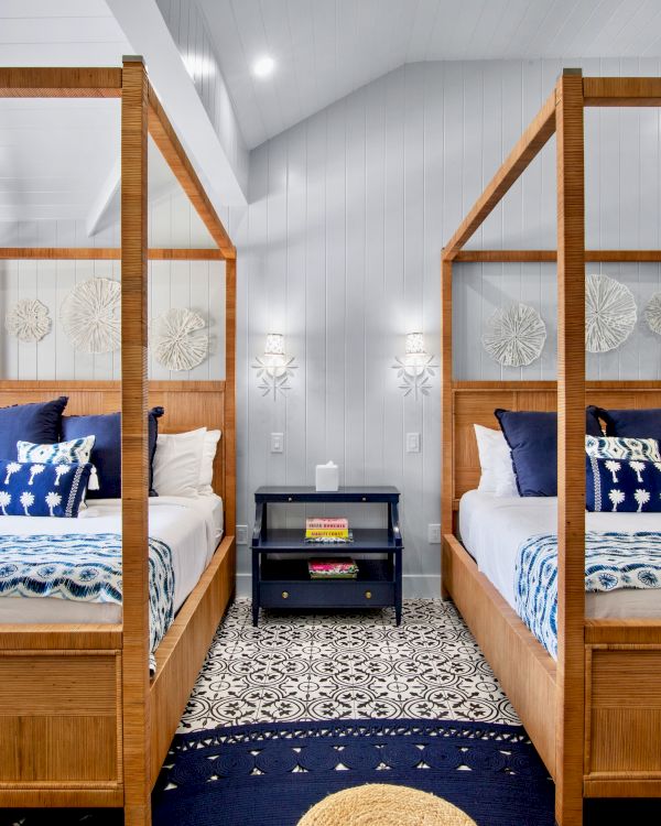The image shows a bedroom with two wooden canopy beds, blue accents, patterned bedding, a central nightstand, and decorative wall hangings.